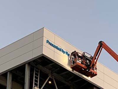 Workers on a crane installing a sign on a tall building.