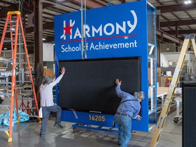 Two men load a large monument sign with a digital display for the Houston School of Achievement.