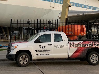 A pickup truck with National Signs decals onsite for a sign installation.